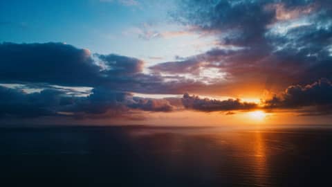 The sun is setting over the ocean on a cloudy day