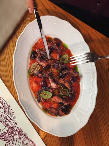 Elegant grilled octopus dish with tomato and olives on a wooden table setting.