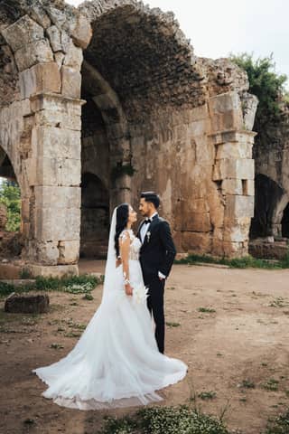 Bride and groom embrace before ancient stone arches, creating a romantic and timeless scene.