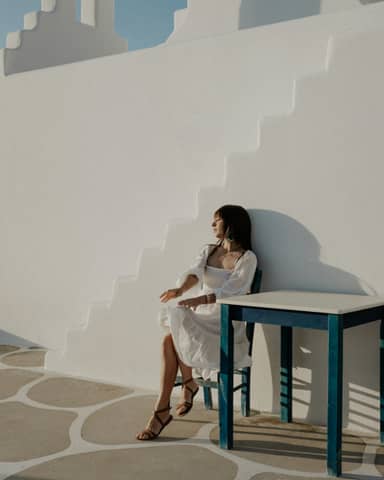 Woman in white dress sits near white wall.
