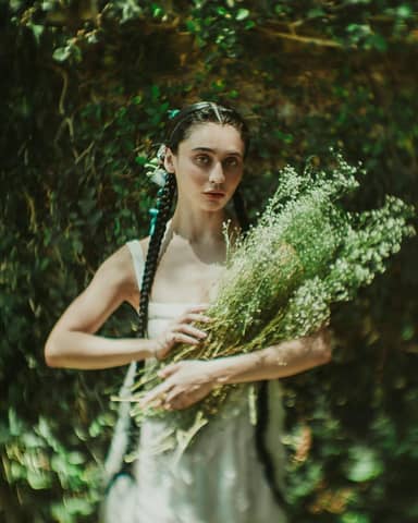 Enchanting portrait of a woman with braids holding delicate wildflowers in a lush green setting.
