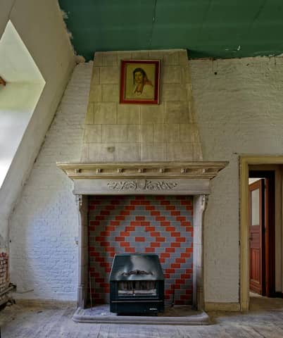 Old fireplace with colorful tiles in a rustic, weathered interior with vintage art framed above.