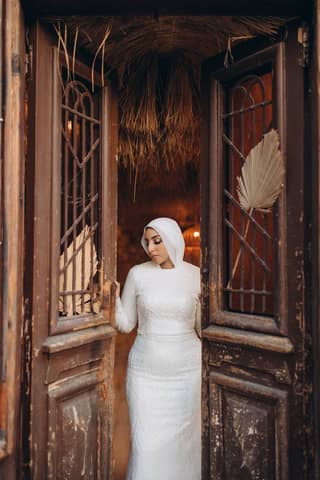 A woman in a white dress stands gracefully between rustic wooden doors.