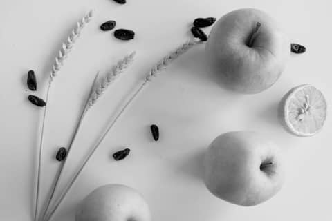 Black and white still life featuring apples, a halved lemon, wheat stalks, and raisins.