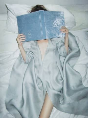 Woman in silk robe reading a book in bed, creating a serene and cozy atmosphere.