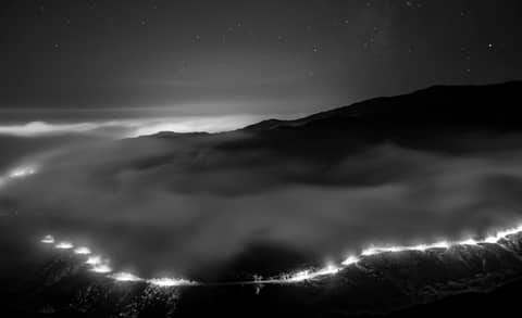 A breathtaking black and white landscape with mist covering hills under a starry night sky.