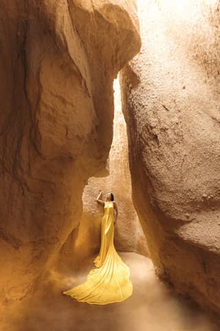 A woman in a striking yellow dress poses confidently amid towering rock formations in Türkiye.