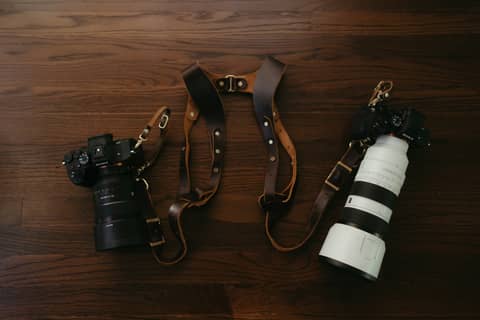 Cameras and a leather camera strap on wood.