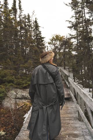Individual on a wooden path through a snowy forest, wrapped in a heavy coat, evoking solitude and adventure.