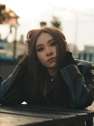 A young woman posing thoughtfully outdoors in a leather jacket, during daytime.