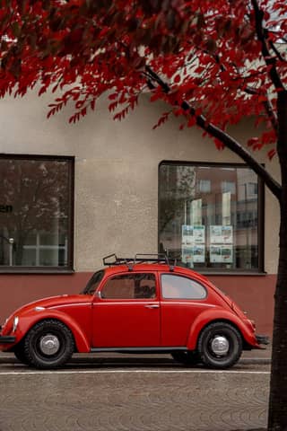 Red vintage Volkswagen Beetle parked under autumn trees in Jönköping, Sweden.