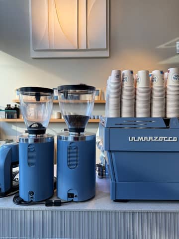 Blue coffee grinders and espresso machine with cups in a chic cafe setting.
