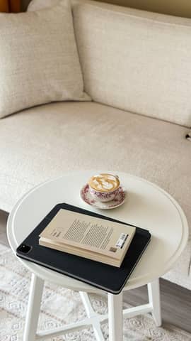 White table with a coffee cup, book, and tablet in a cozy living room setting.