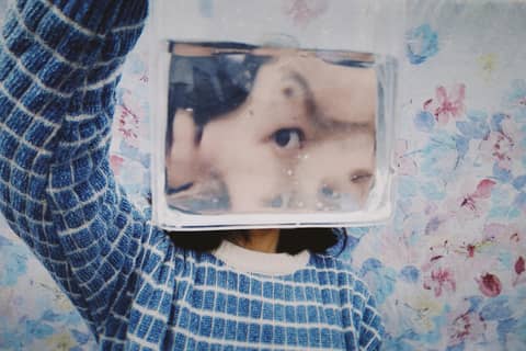 Artistic portrait showing a woman's reflection distorted through a glass water container over a floral background.