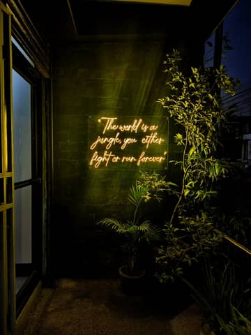 Neon text in a dark corner creates a moody atmosphere with plants.