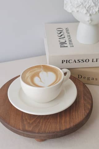 A cup of espresso with latte art on a wooden tray beside art books in a cozy setting.