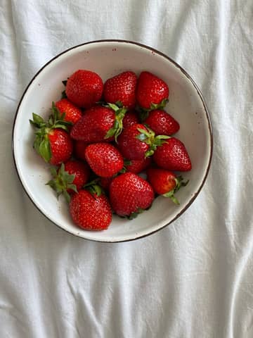 A vibrant bowl of fresh strawberries resting on a white surface, perfect for summer.