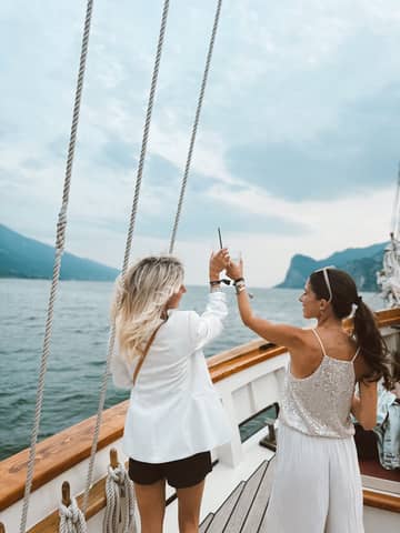 Two stylish women toasting on a yacht cruise in Italy's beautiful lake scenery.