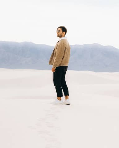 Man standing on white sand, mountains in background.