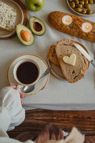 Cozy breakfast scene with coffee, bread, and avocado on a rustic table.