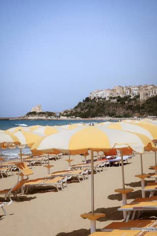 Picturesque beach scene with yellow umbrellas and a coastal village in the background.