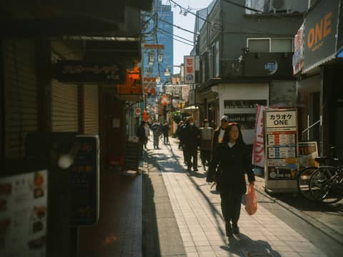 People stroll down a busy, sunlit tokyo street.