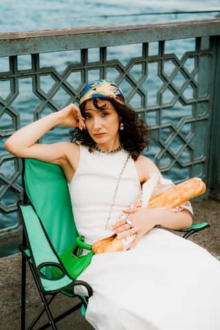 Stylish woman sitting by riverside holding a baguette. Urban tranquility captured.