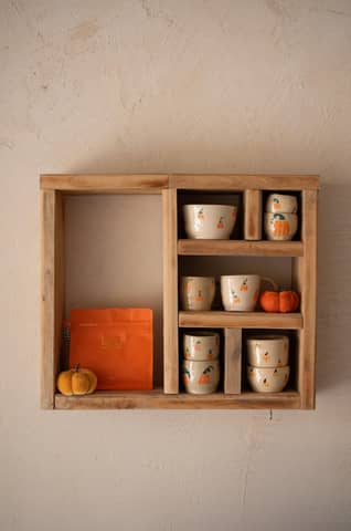 Wooden shelf displaying ceramic cups and mini pumpkins, evoking an autumnal feel.