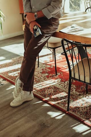 Stylish person leaning on table indoors holding vintage camera in warm sunlight.