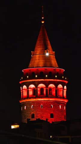Striking night view of Galata Tower glowing red under the dark sky.