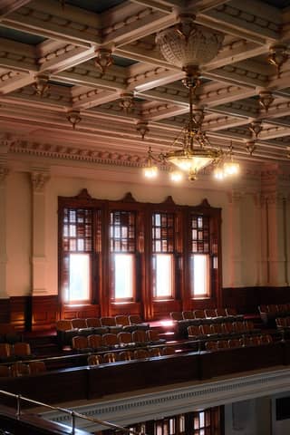 Sunlit antique woodwork and seating in the Texas State Capitol's historic chamber.
