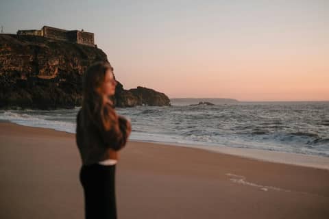 Silhouette of a woman gazing at a coastal sunset near the cliffs of Nazare, Portugal.