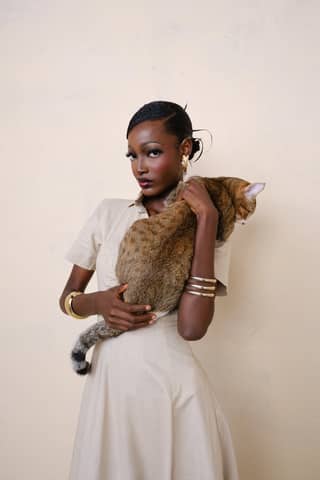 Stylish woman holding a cat in a minimalist setting, exuding poise and elegance.