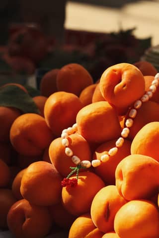 A close-up of ripe apricots adorned with a delicate beaded necklace, bathed in sunlight.