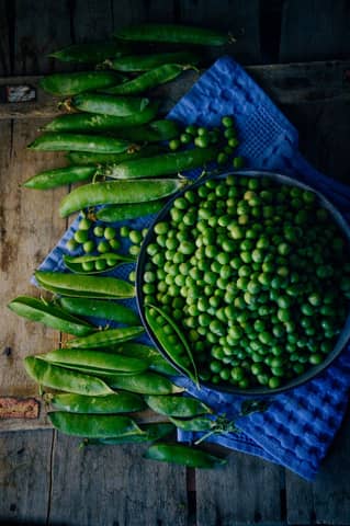 An artistic arrangement of fresh green peas and pods on a rustic wooden surface with a blue cloth.