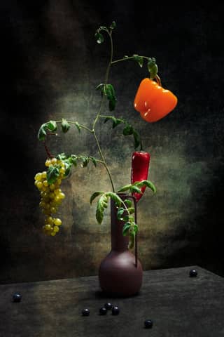 A creative arrangement of bell peppers and grapes in a vase, showcasing artistic still life.