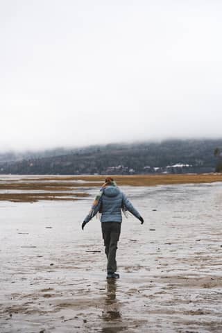 A person strolls alone on a scenic, misty beach with distant mountains.