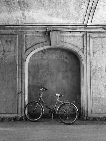 Vintage bicycle leaning against an arched wall in a rustic setting. Black and white.