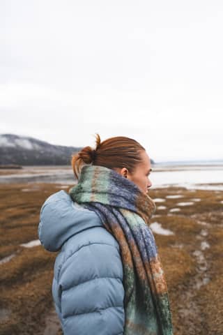 Side view of a woman in a blue jacket and scarf at a misty beach, capturing a serene moment.
