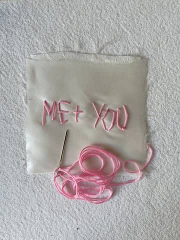 Pink thread embroidery on white fabric with 'Me + You.'