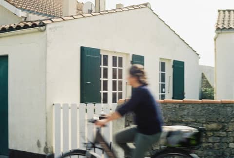 A blurred cyclist passes by a quaint cottage in Nuova Aquitania, France, showcasing rustic charm.