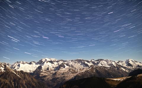 A view of a mountain range with a star trail in the sky