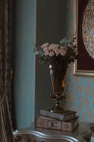Vintage interior with elegant floral vase and antique books on ornate table.