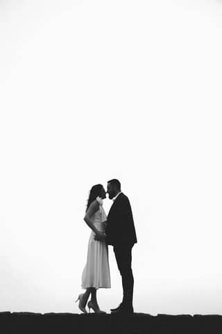 Black and white silhouette of a couple embracing and kissing outdoors, capturing a romantic moment.