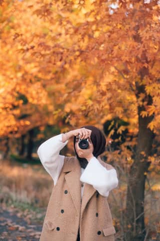 A woman taking photos amidst vibrant autumn leaves, showcasing the beauty of fall.