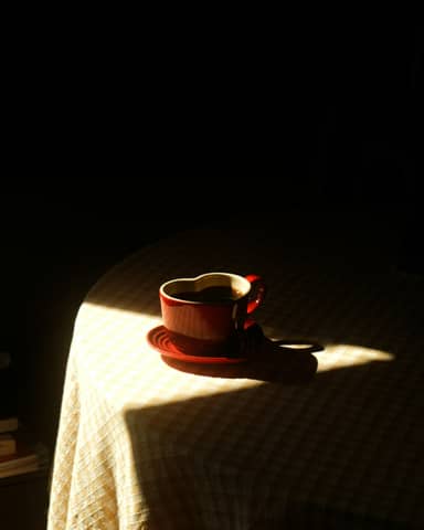 A red heart-shaped coffee cup sits in sunlight.
