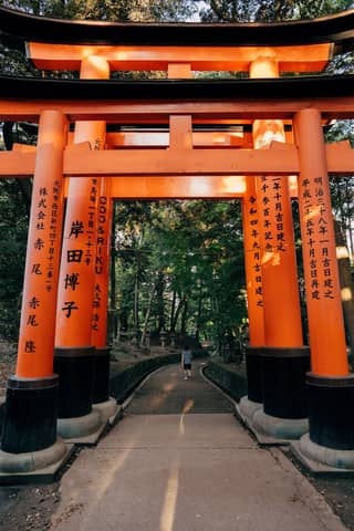 A vibrant Torii gate at Fushimi Inari Shrine in Kyoto, surrounded by lush greenery.