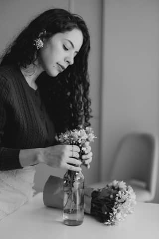 Black and white photo of a woman arranging flowers in a vase indoors.