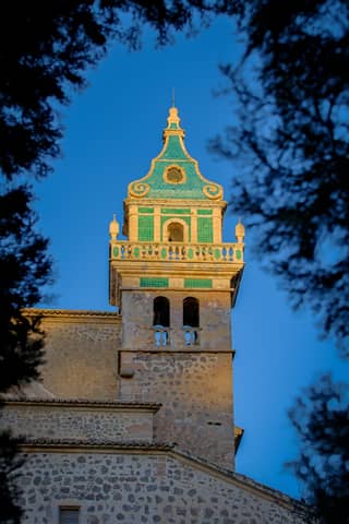 Beautiful view of Valldemossa Charterhouse tower captured at sunset, framed by trees.
