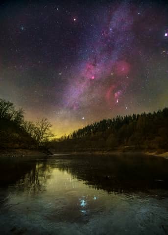 The night sky is filled with stars above a lake